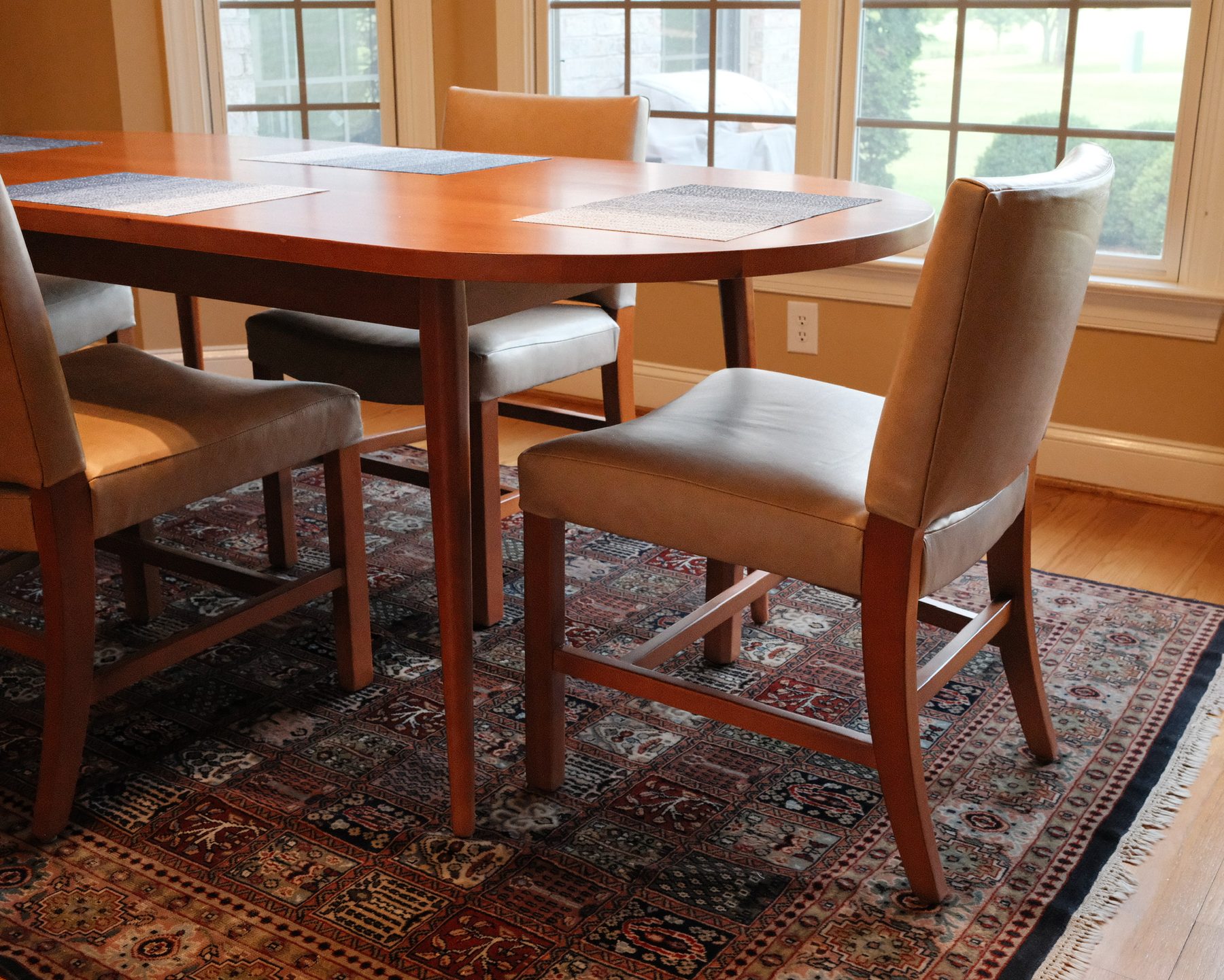 Oval wood dining table with leather-seat chairs on a patterned rug