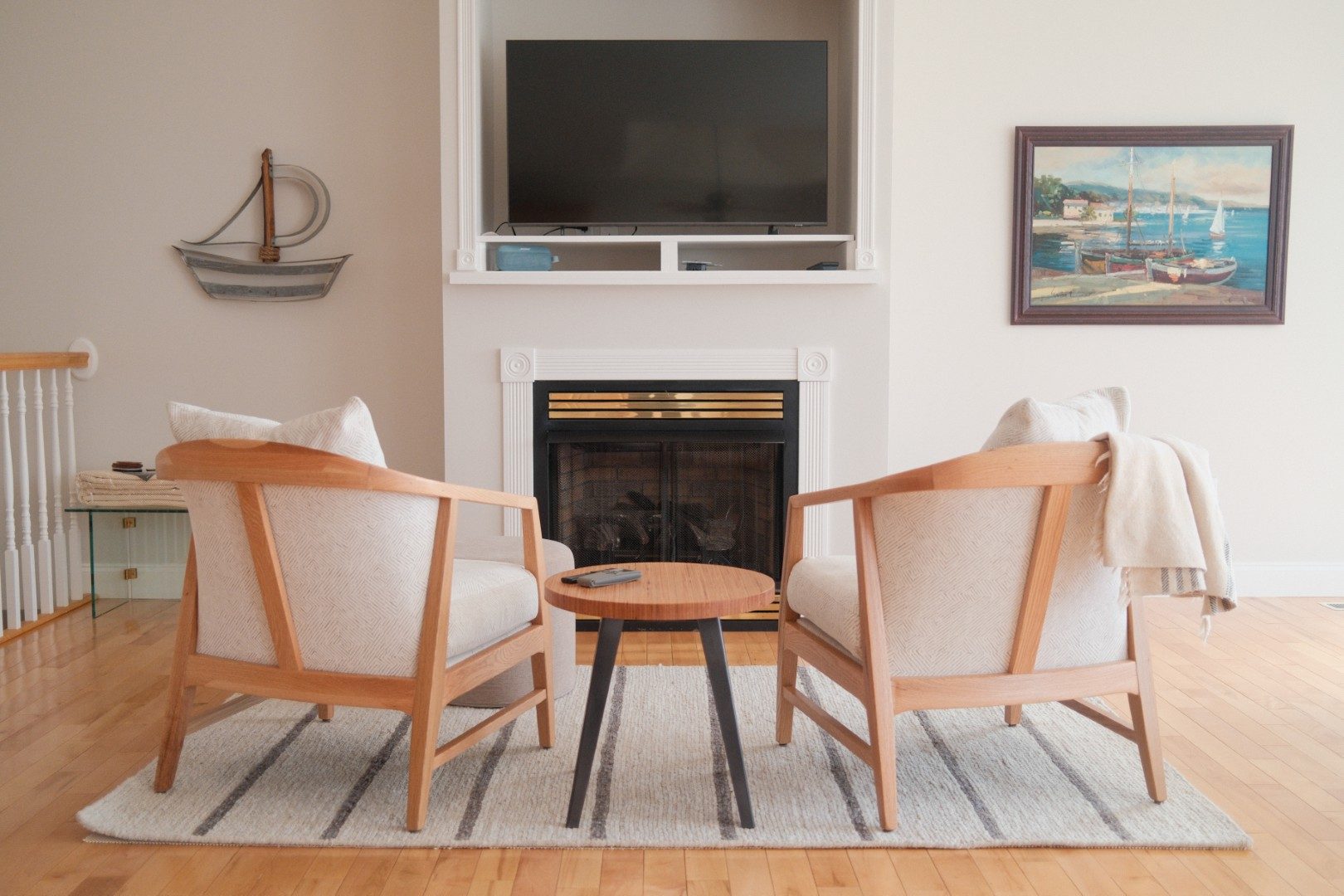 Two wood-framed lounge chairs and a round side table facing a fireplace