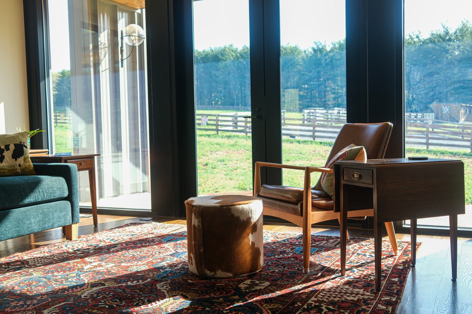 Leather lounge chair, cowhide ottoman and side table on a red patterned rug by tall windows