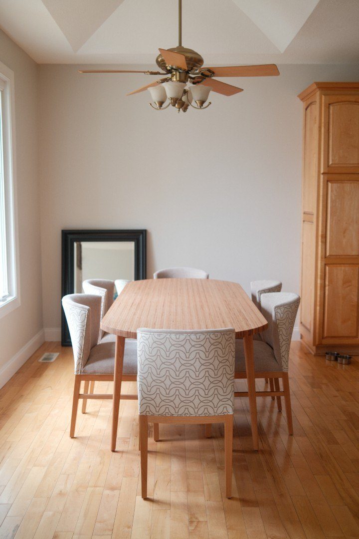 Oval wood dining table with six patterned upholstered chairs on a maple floor