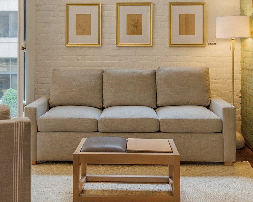 Three-seat oatmeal sleeper sofa under three framed prints with a wood coffee table in front