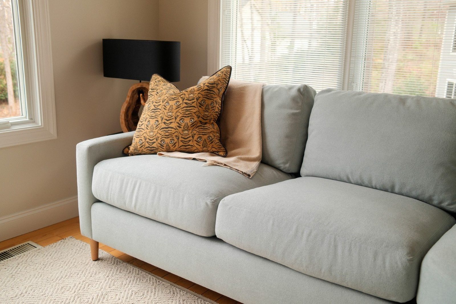 Light gray-blue sofa with a tiger-print pillow and blanket by a sunny window